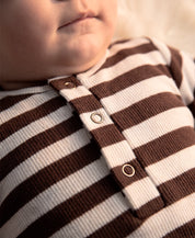 Conjunto Body + Calça Canelada Bebê Listras Marrom MiniMalista Baby — pose lifestyle do bebê no aconchego do inverno, algodão canelado 100% respirável antialérgico, escala granular do RN aos 18-24 meses.