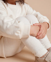 MiniMalista Conjunto Moletom + Calça Canelada em Branco Off vista costas. Moletom oversized soltinho + calça canelada slim, look infantil monocromático unissex, estética escandinava minimalista para bebê e criança.